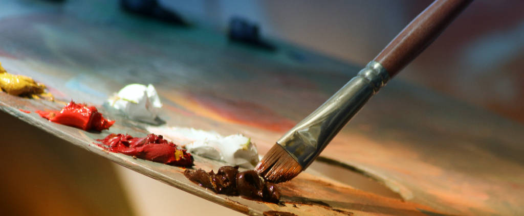 Painter's palette with white, red, yellow and brown color. Painter soaks brush in a paint