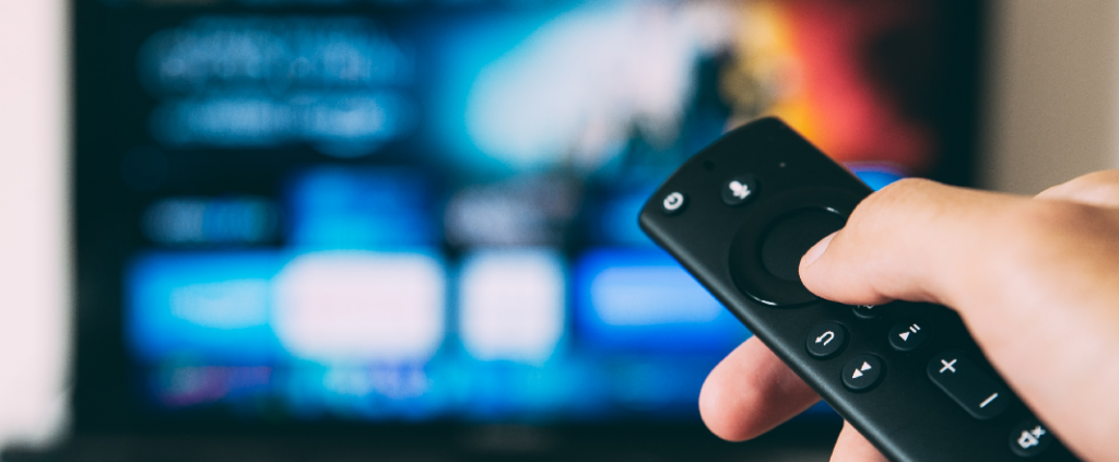 Remote controller pointing at blurred tv with video library