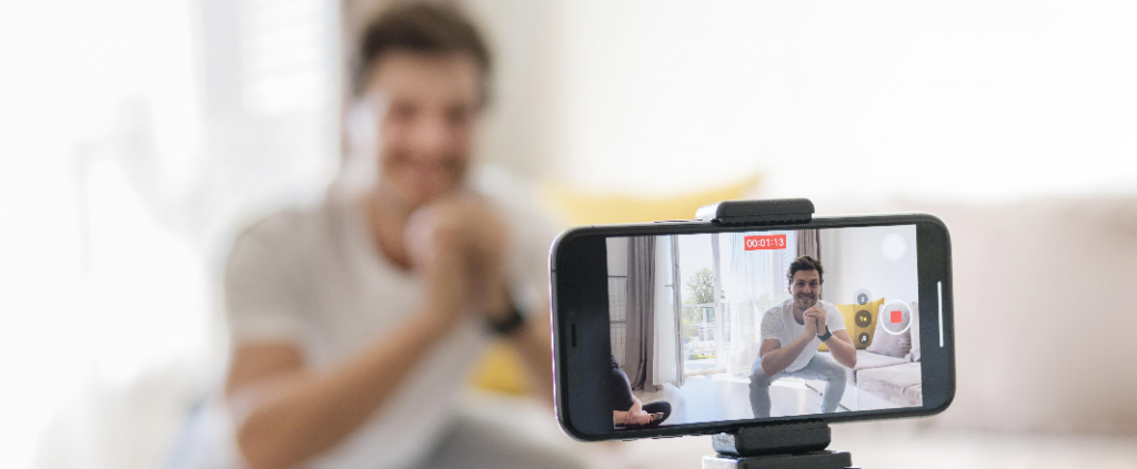 Man in white shirt records himself on a mobile while doing a squat