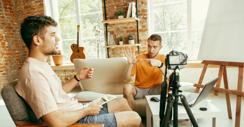 Two adults recording Youtube video in living room sitting on couch