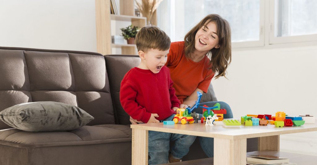 Kid playing with plastic building kit while mom smiling at him