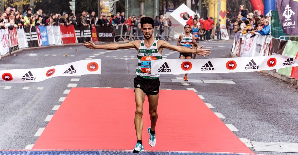 Man crossing marathon finish line as a first cutting ribbon in half